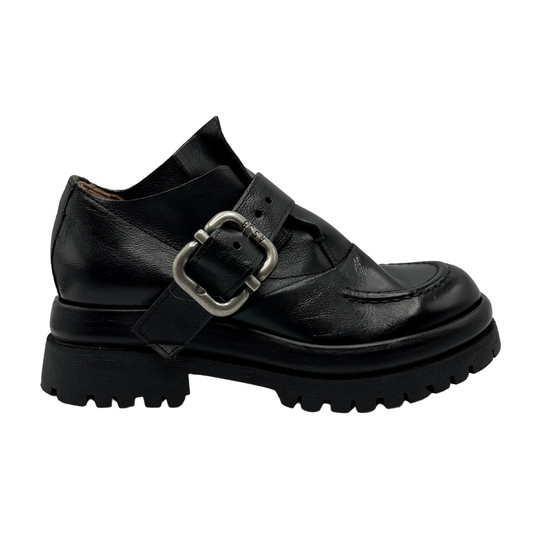 Right facing view of black leather shoe with large buckle, thick lug sole and rounded toe