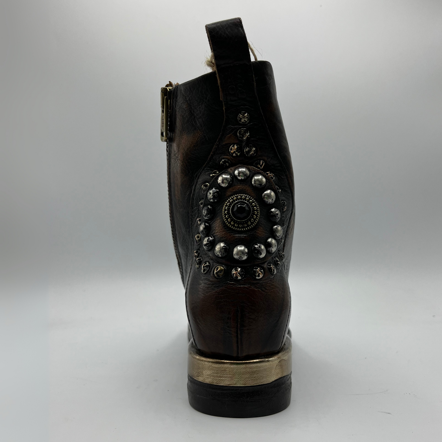 Back view of a brown and black burnished short boot with a gold accent on the heel and metallic embellishments along the shaft.