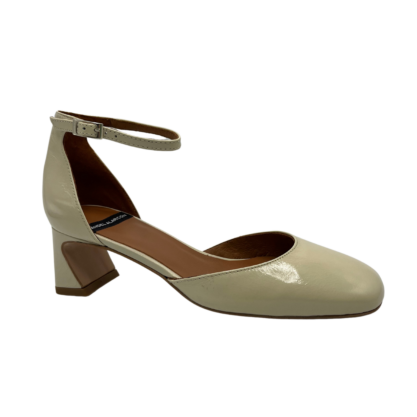 45 degree angled view of a patent leather pump in off white. Featuring a delicate ankle strap, rounded toe and flared block heel.