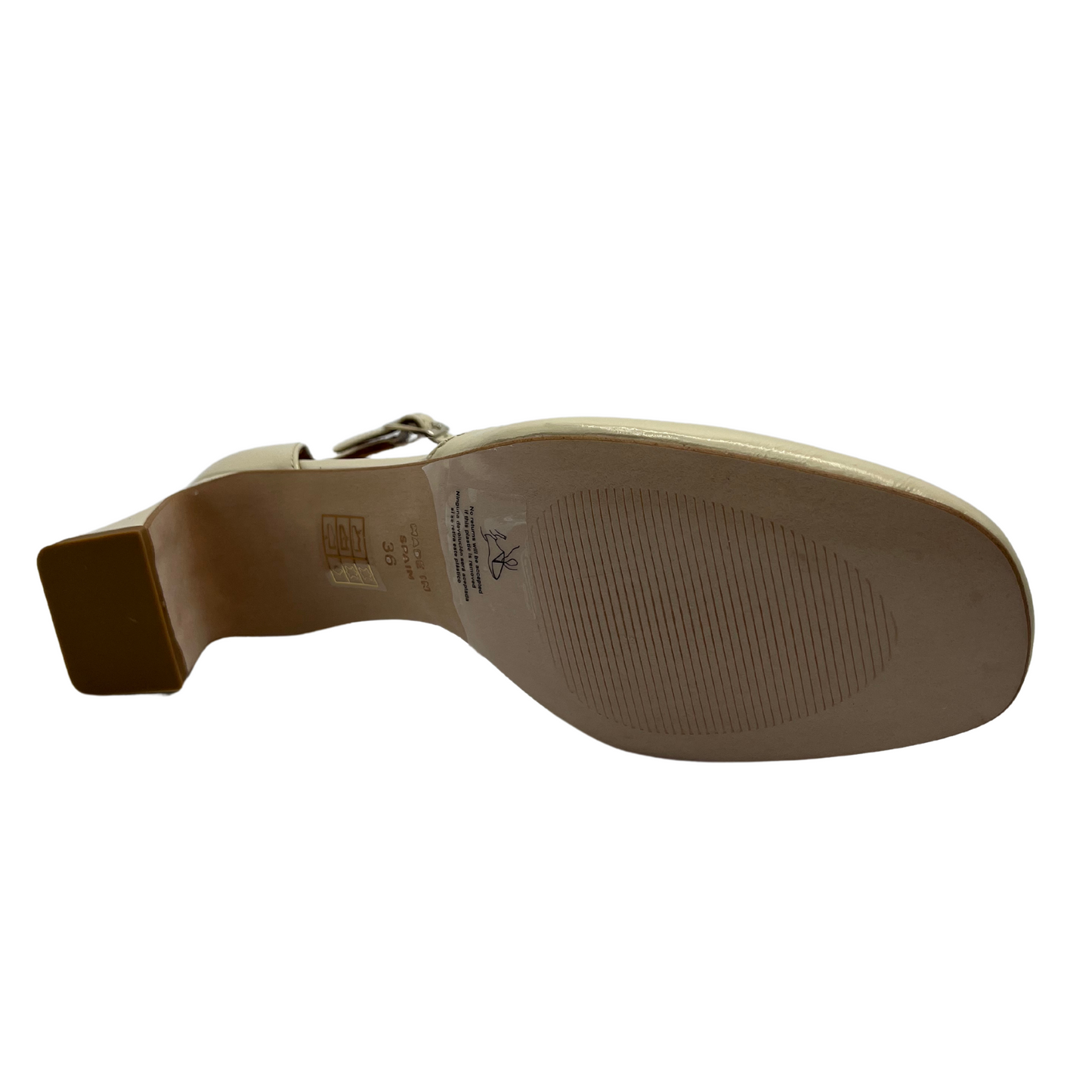Bottom view of a patent leather pump in off white. Featuring a delicate ankle strap, rounded toe and flared block heel.