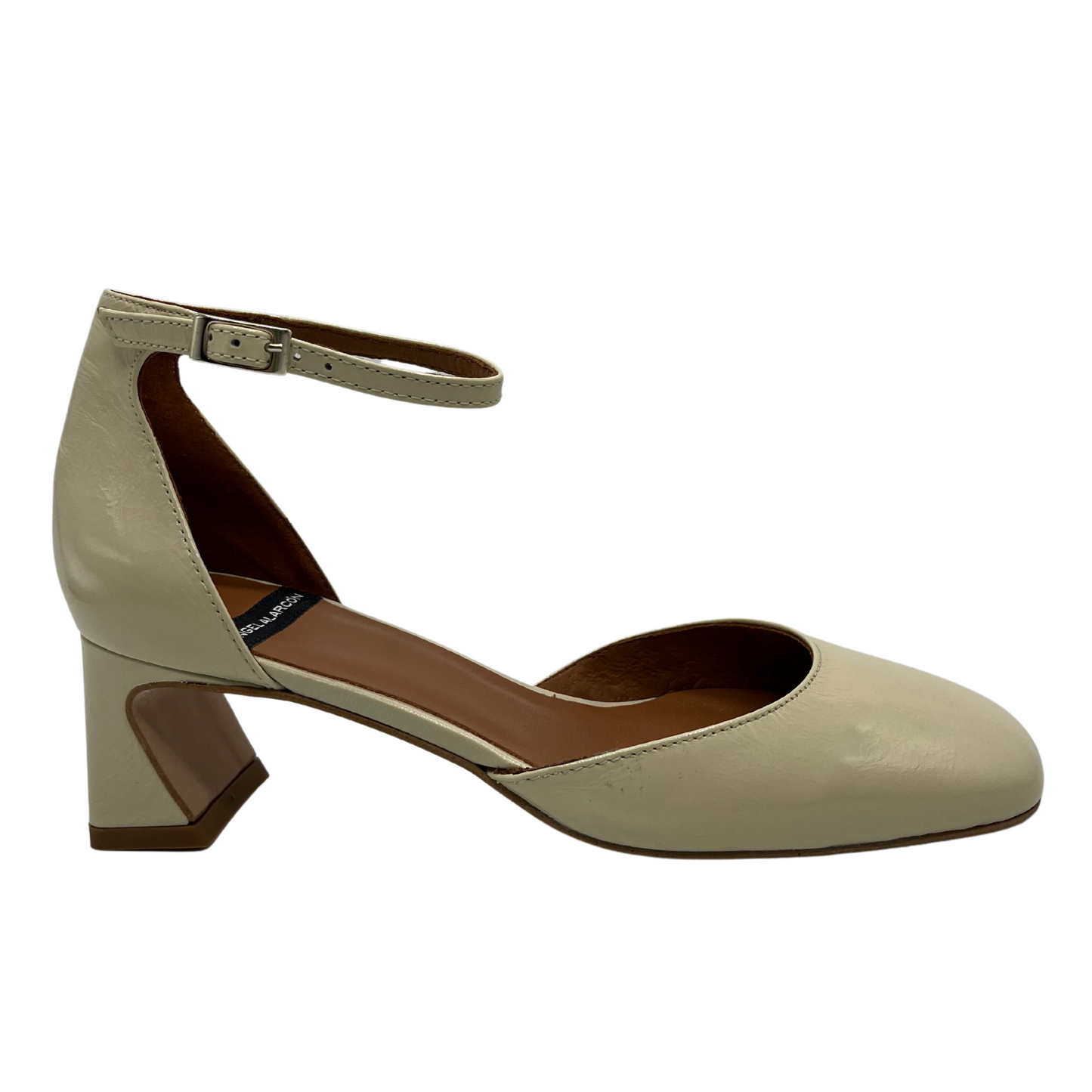 Right facing view of a patent leather pump in off white. Featuring a delicate ankle strap, rounded toe and flared block heel.