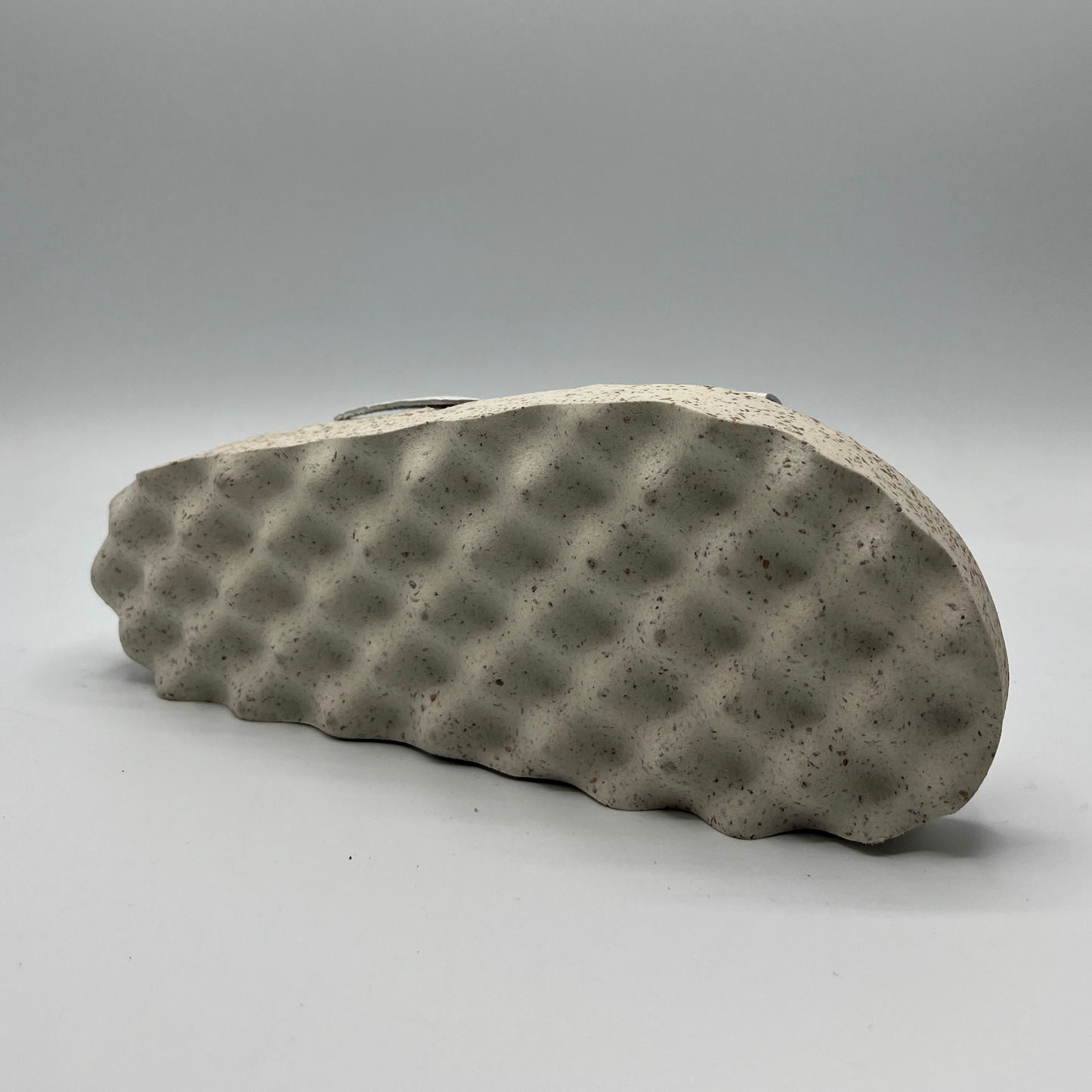 Bottom view of double strap white faux leather sandal with a contoured footbed and thick white and brown speckled outsole.