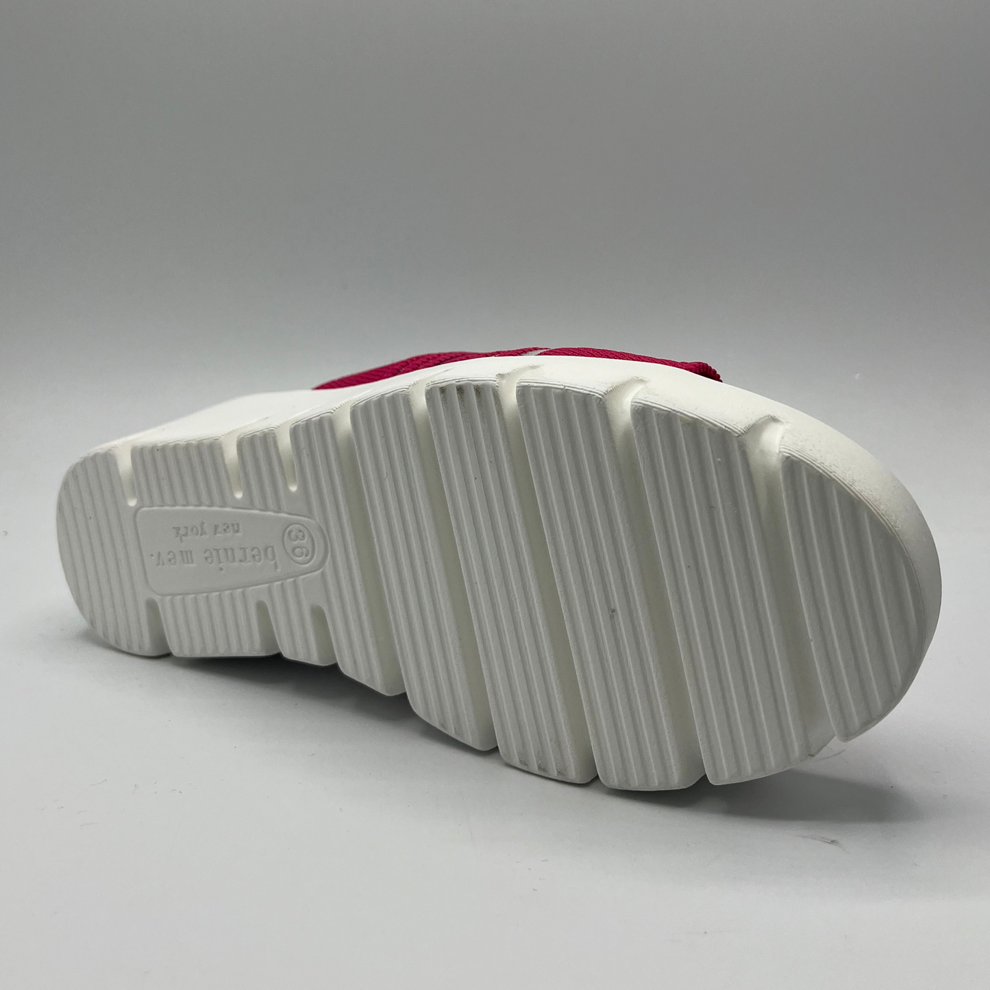 Bottom view of a fuschia elastic slip on sandal with a white wedge heel.