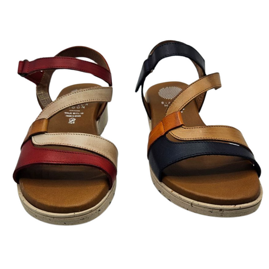 Front view of two leather sandals side by side. The left one is red, cream and brown and the right one is navy, tan and orange. Both have an open toe, velcro ankle strap and a lined footbed