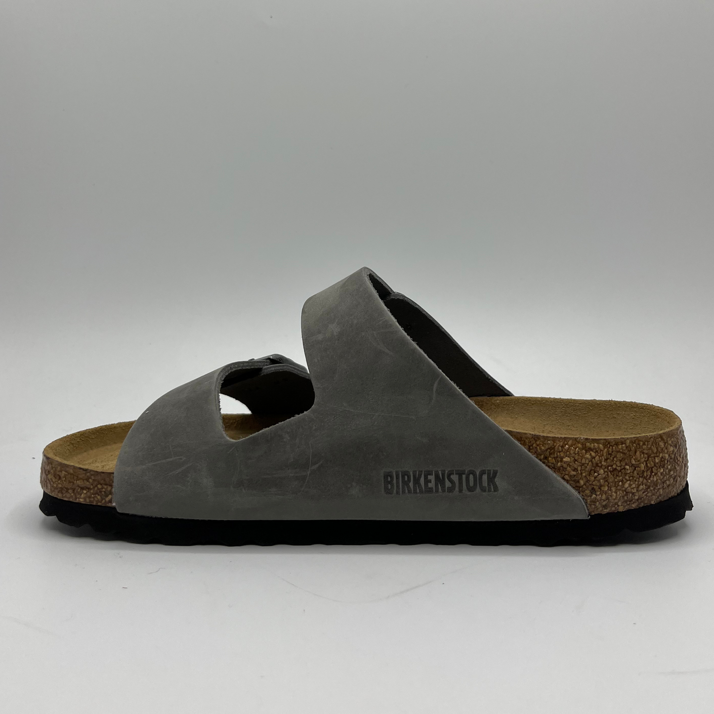 Left facing view of an iron coloured leather sandal with a contoured cork footbed and two adjustable straps.