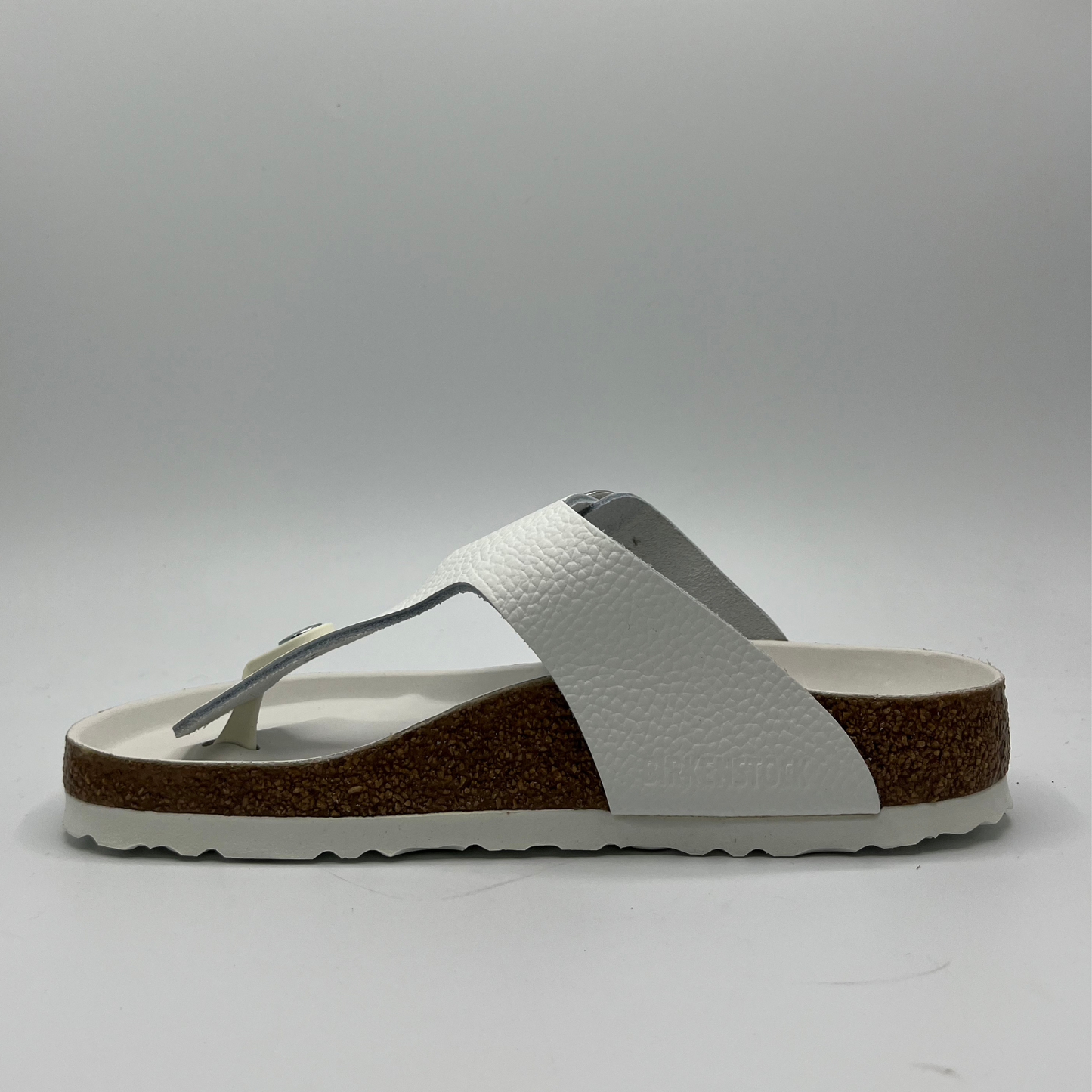 Left facing view of a white leather thong sandal with a big silver buckle on the adjustable strap. Featuring a contoured cork footbed with a leather lining.