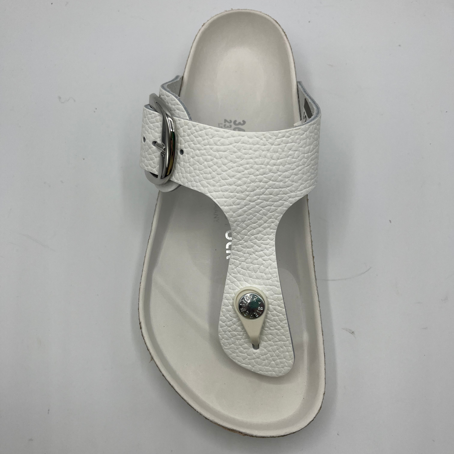 Top view of a white leather thong sandal with a big silver buckle on the adjustable strap. Featuring a contoured cork footbed with a leather lining.