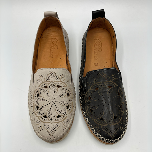 Top view of two leather slip on shoes with a laser cut design on the uppers. Hand stitched details connecting the upper to the outsole. Pull on heel tab and leather lined.