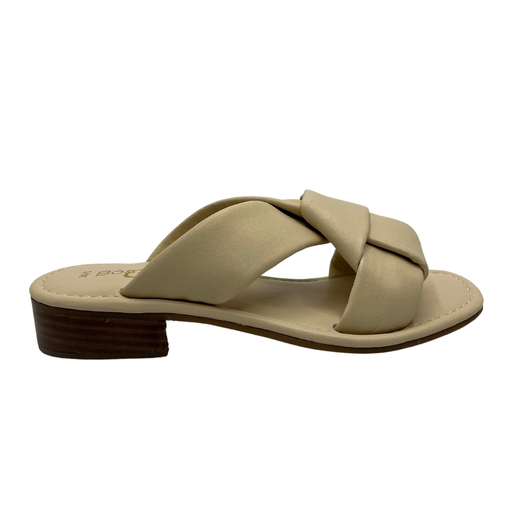 Right facing view of cream leather sandal with short block heel and large knot detail on straps.