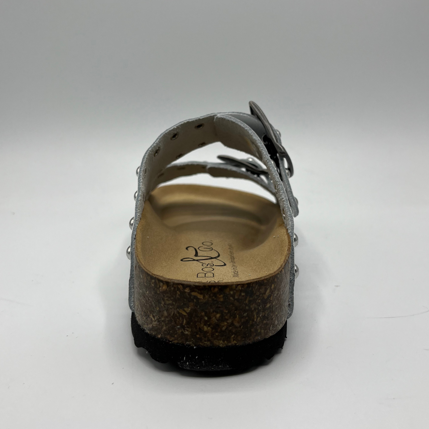 Back view of a white leather sandal with a contoured cork footbed. Featuring adjustable buckle straps and silver stud details.