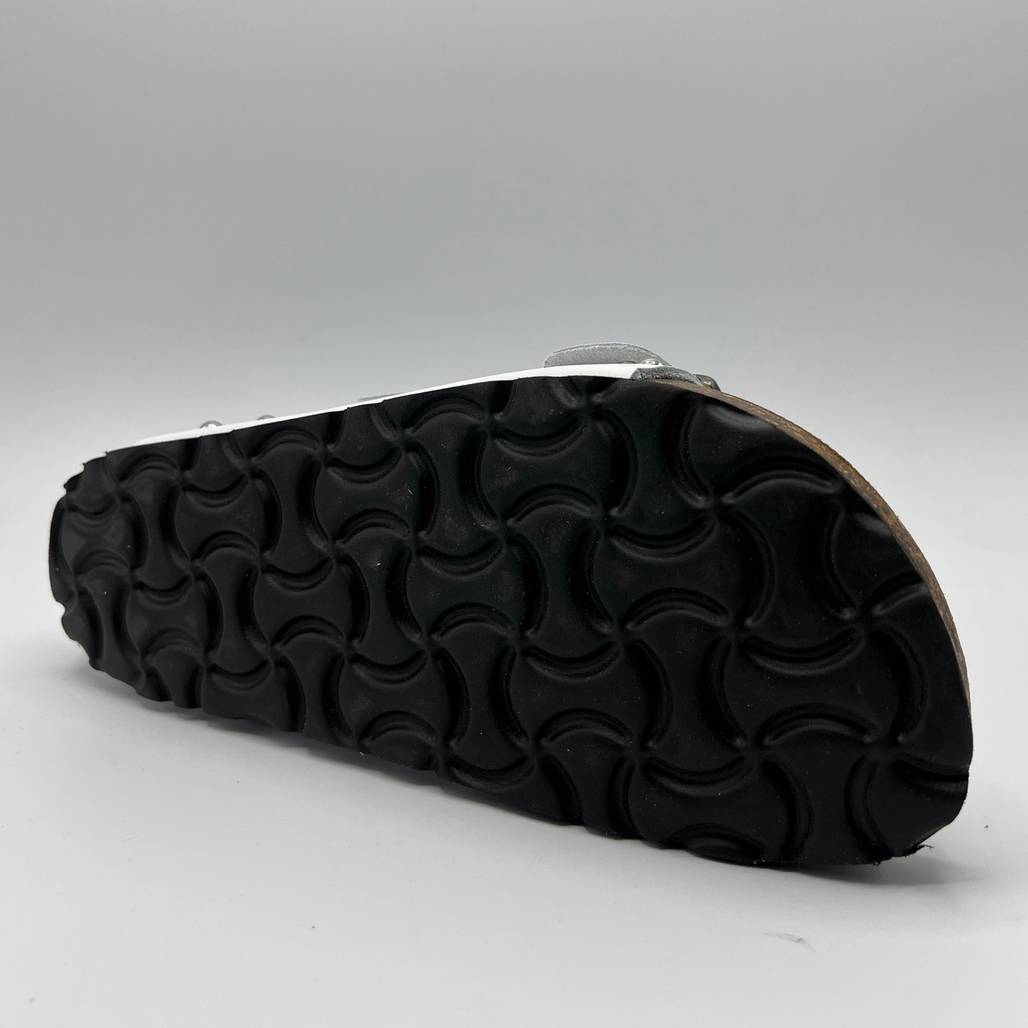 Bottom view of a white leather sandal with a contoured cork footbed. Featuring adjustable buckle straps and silver stud details.