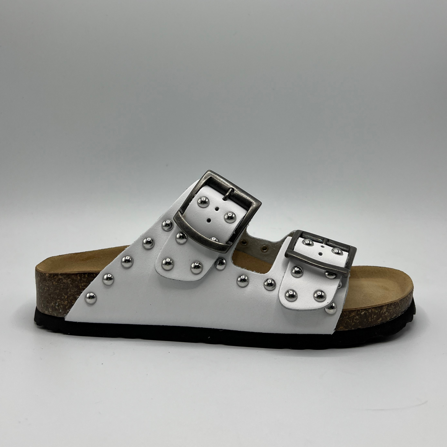Right facing view of a white leather sandal with a contoured cork footbed. Featuring adjustable buckle straps and silver stud details.