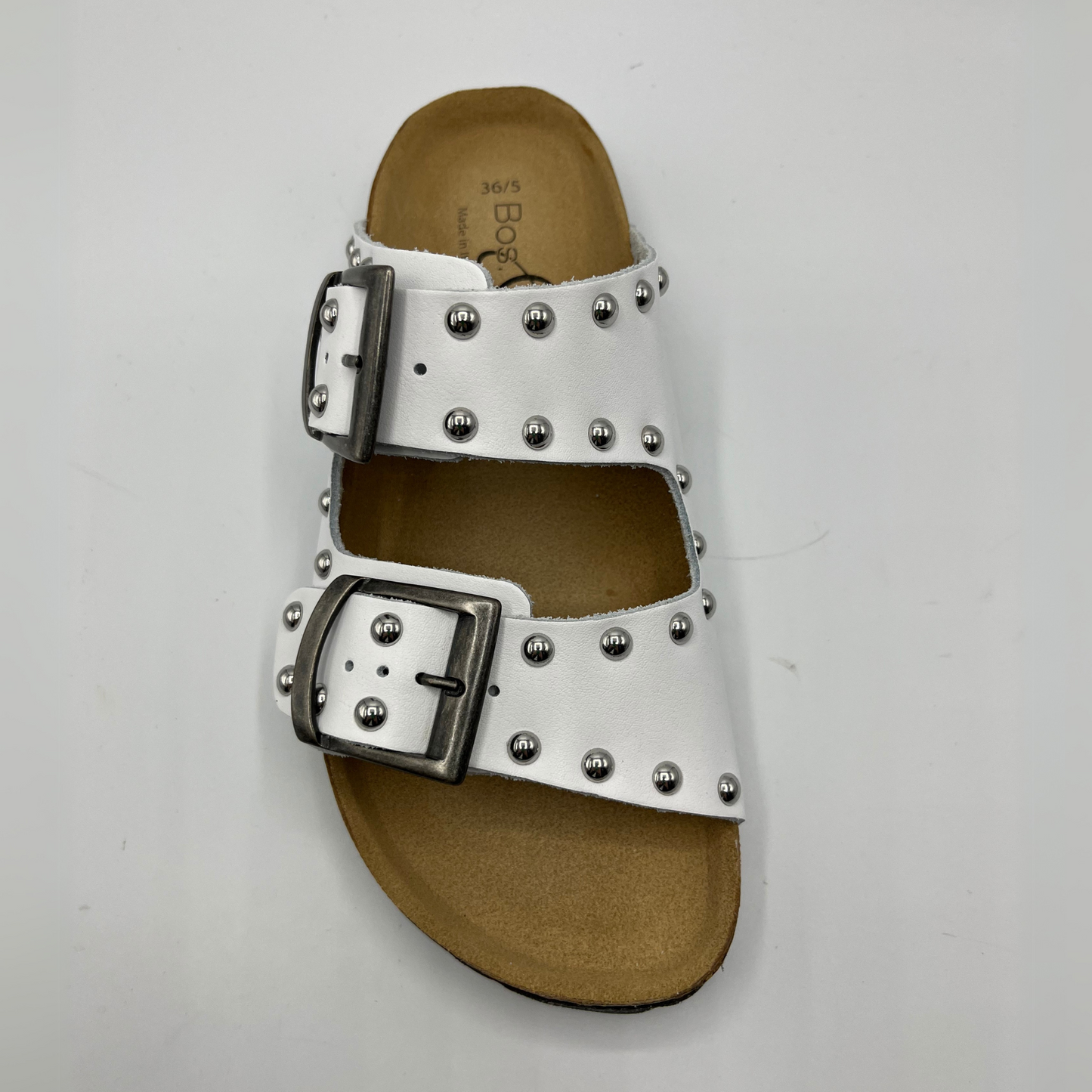 Top view of a white leather sandal with a contoured cork footbed. Featuring adjustable buckle straps and silver stud details.