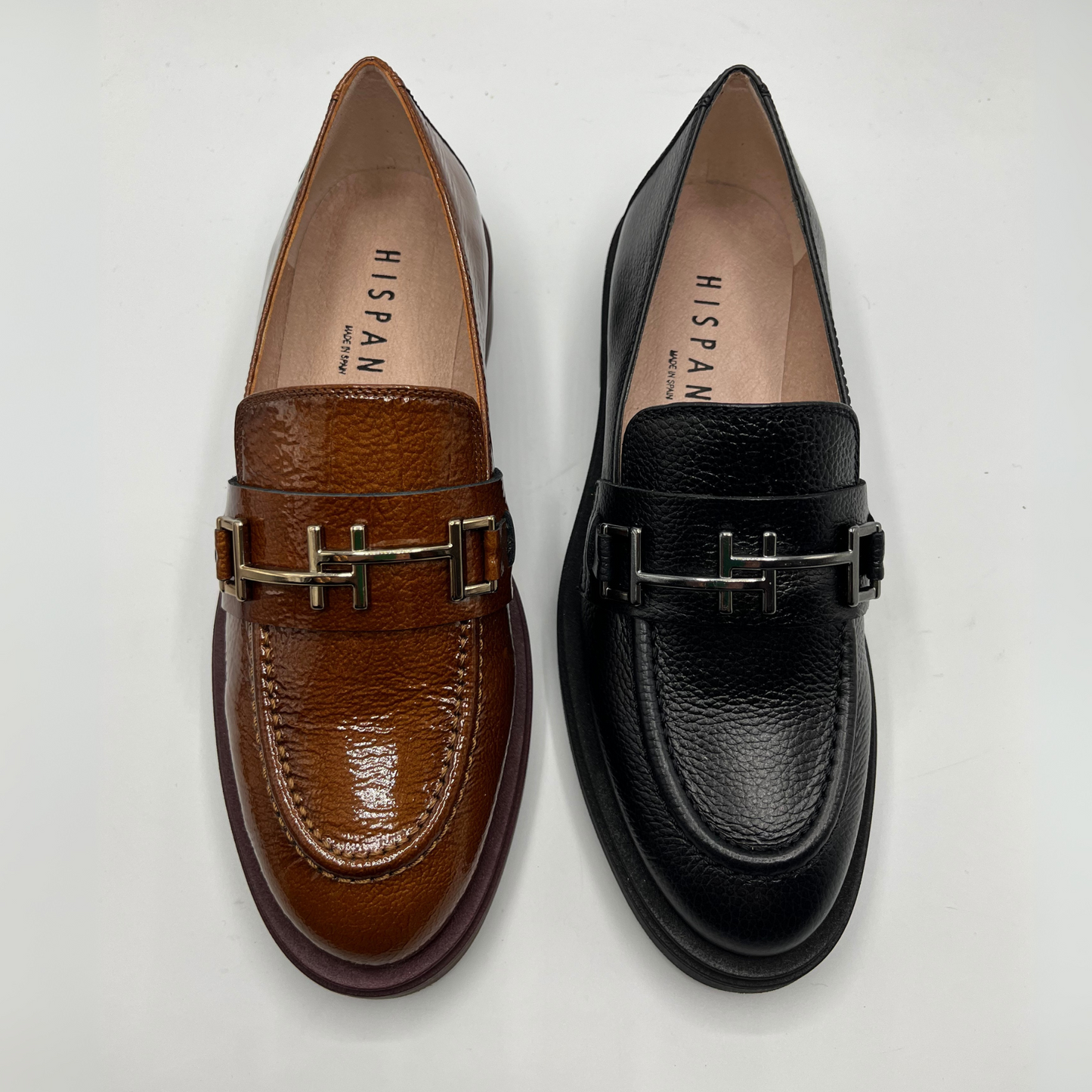 Brown and black loafers with metallic buckles on a white background