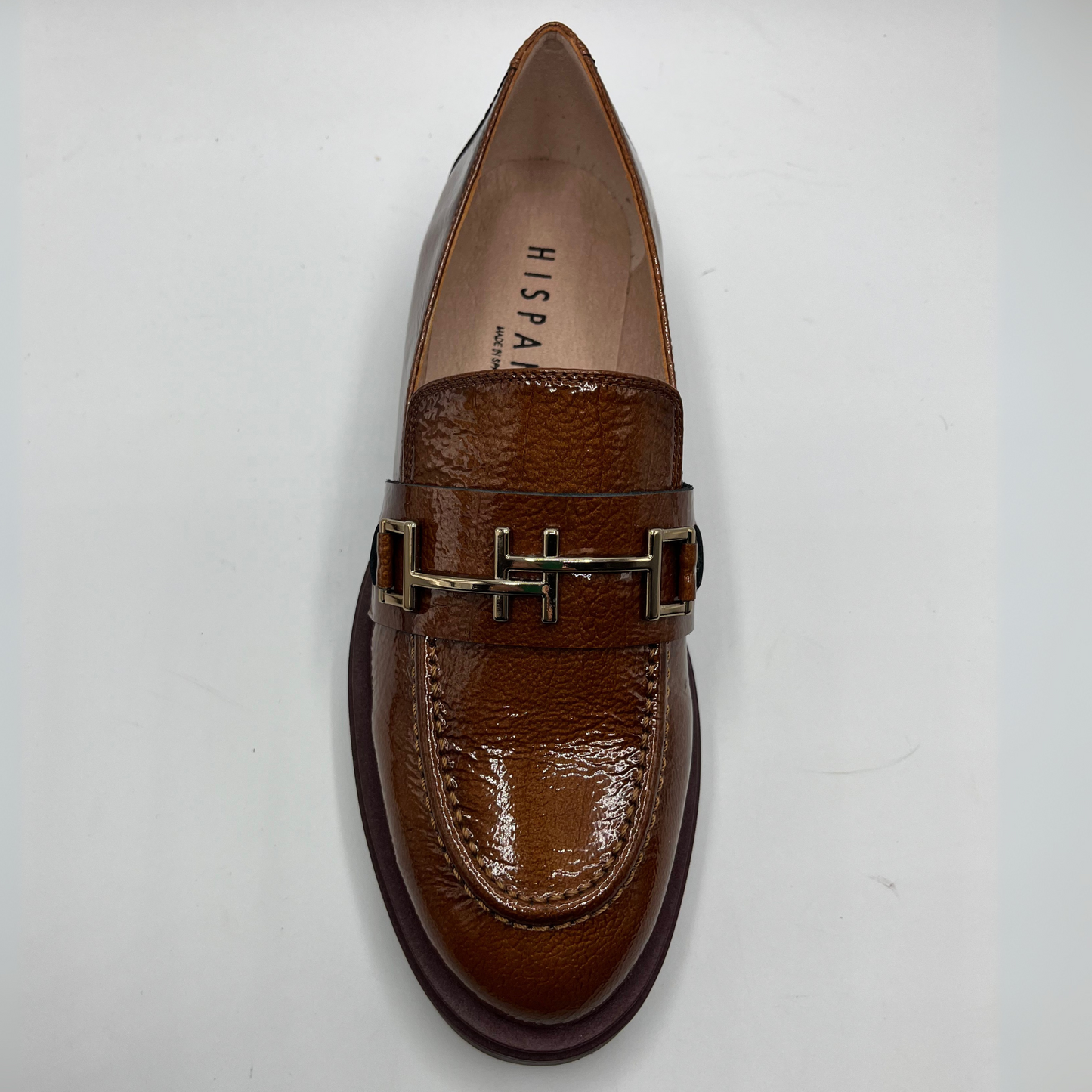 Brown loafer shoe with gold buckle on a white background