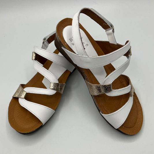 Top view of a pair of white and champagne coloured leather sandals. ZIgzag strap design and a low wedge heel.