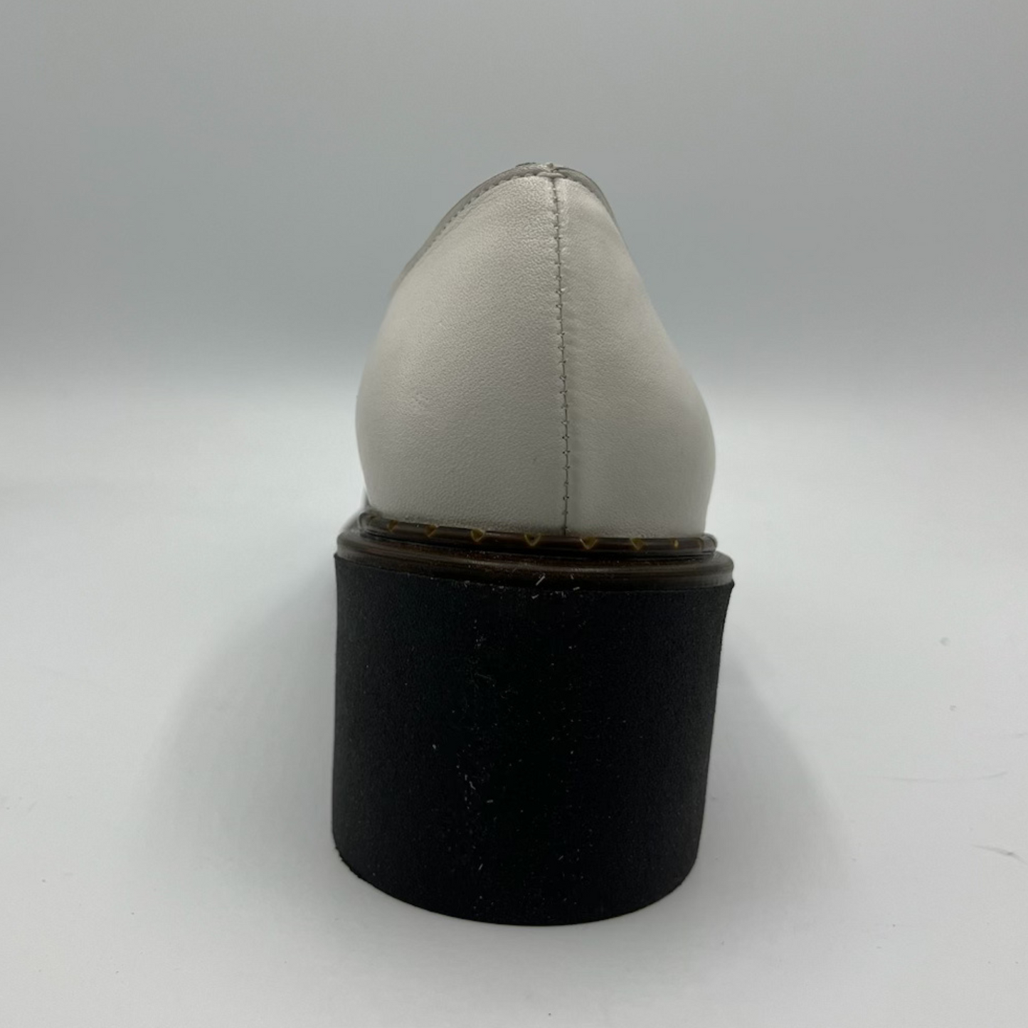White shoe on a black cylindrical stand against a white background