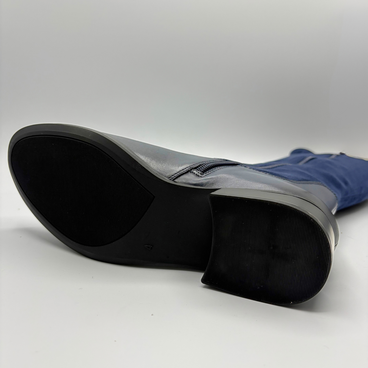 Bottom view of a tall navy boot with an inner zipper closure