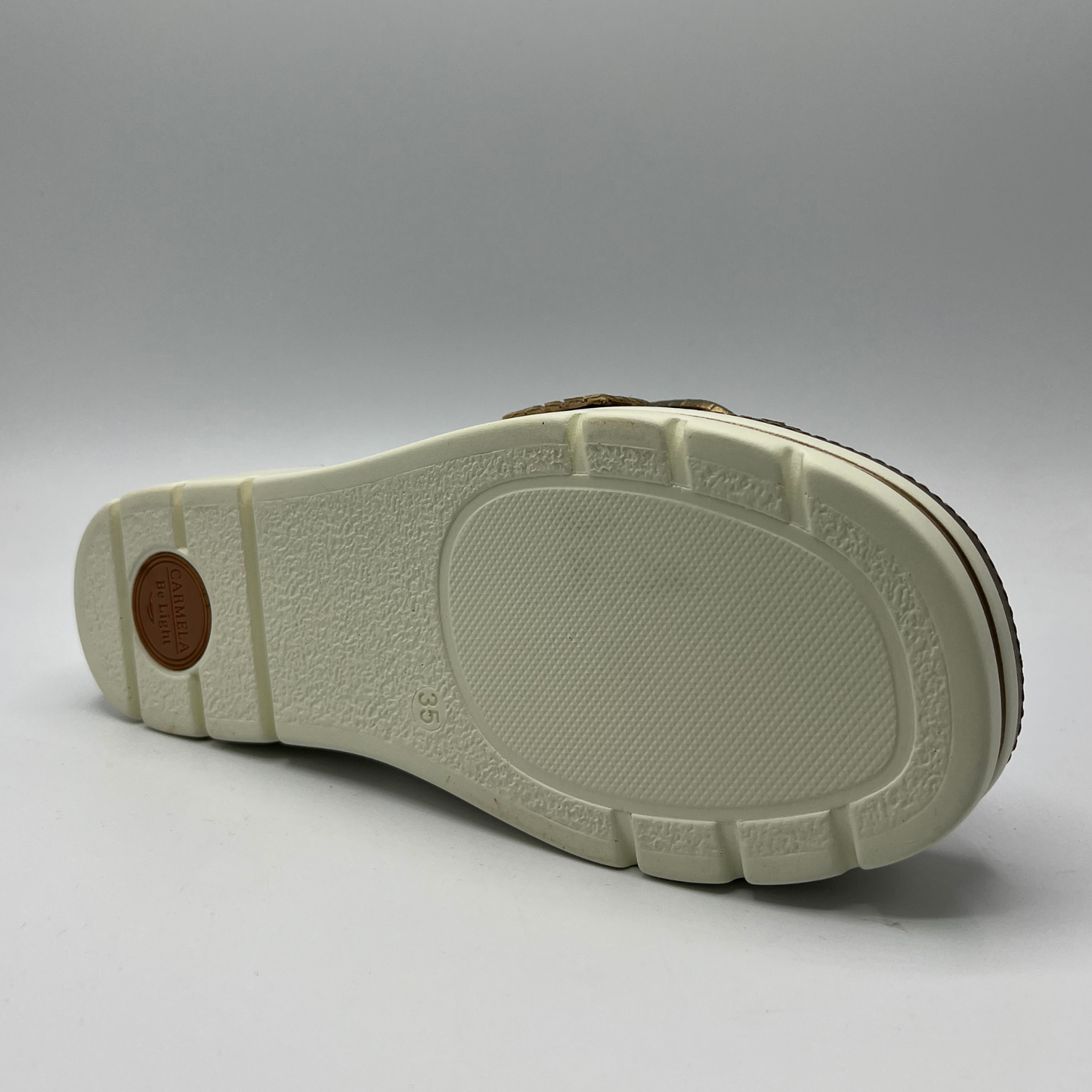 Bottom view of a bronze leather sandal with a white rubber outsole. Featuring a weave design on the strap and a decorative buckle.