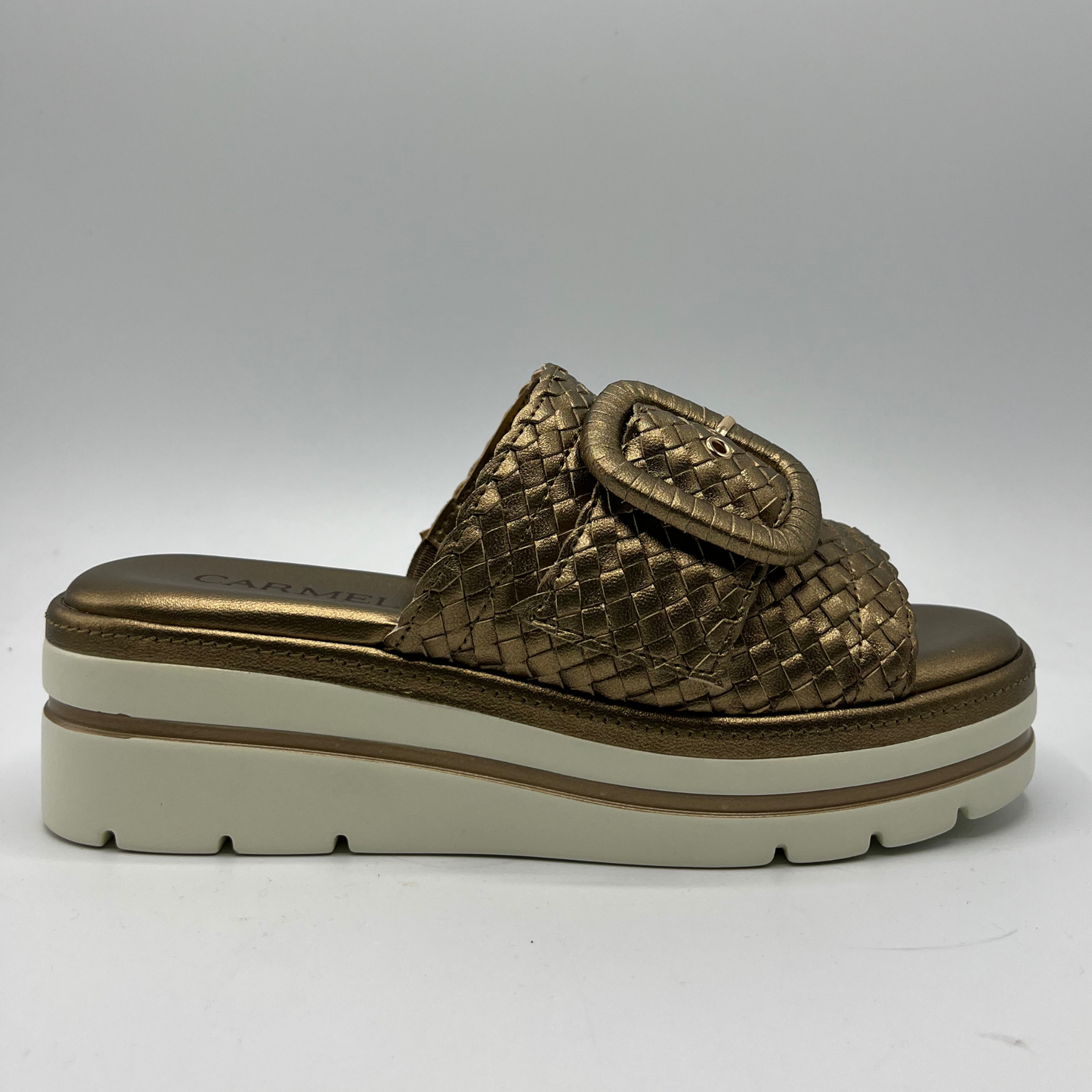 Right facing view of a bronze leather sandal with a white rubber outsole. Featuring a weave design on the strap and a decorative buckle.