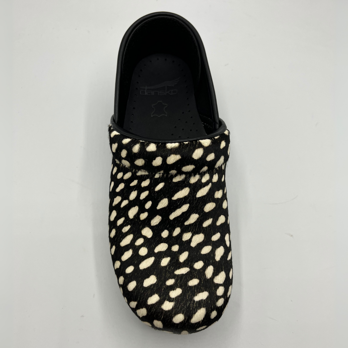 Black slip-on shoe with white polka dot pattern on a light gray background