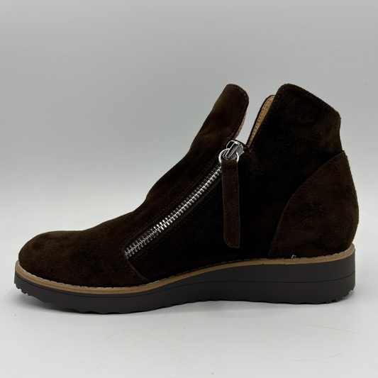 A dark brown suede ankle boot with a side zipper, a pull tab, and a wedge heel, shown in profile against a light gray background.