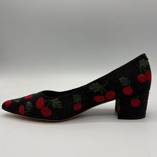 A single black pointed-toe pump with a block heel, covered in a red cherry and green leaf pattern, shown against a neutral gray background.