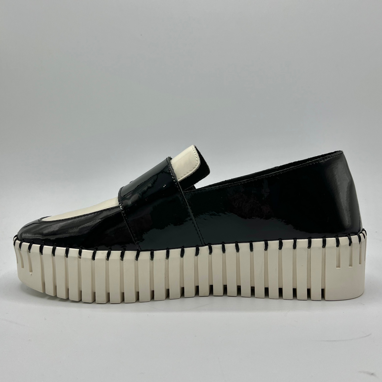 Black patent leather loafer with a thick white sole on a gray background