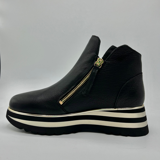 Black platform sneaker with a gold zipper on a light gray background