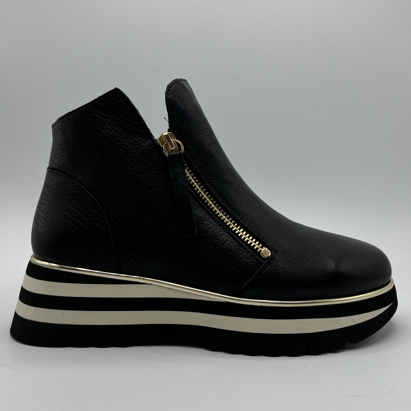 Black platform sneaker with a gold zipper on a grey background