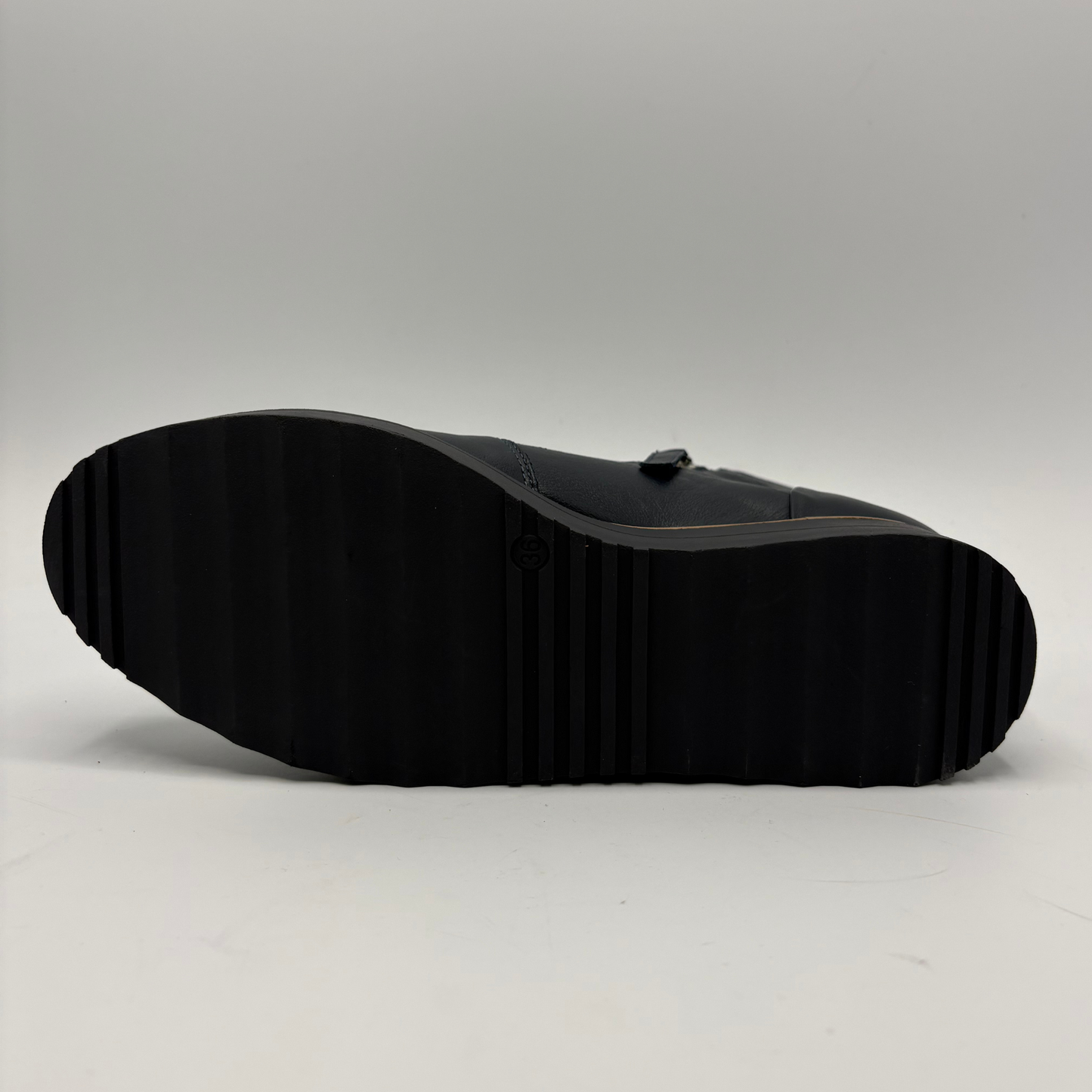 The black rubber outsole of a shoe, shown from a bottom-up perspective against a neutral gray studio background.