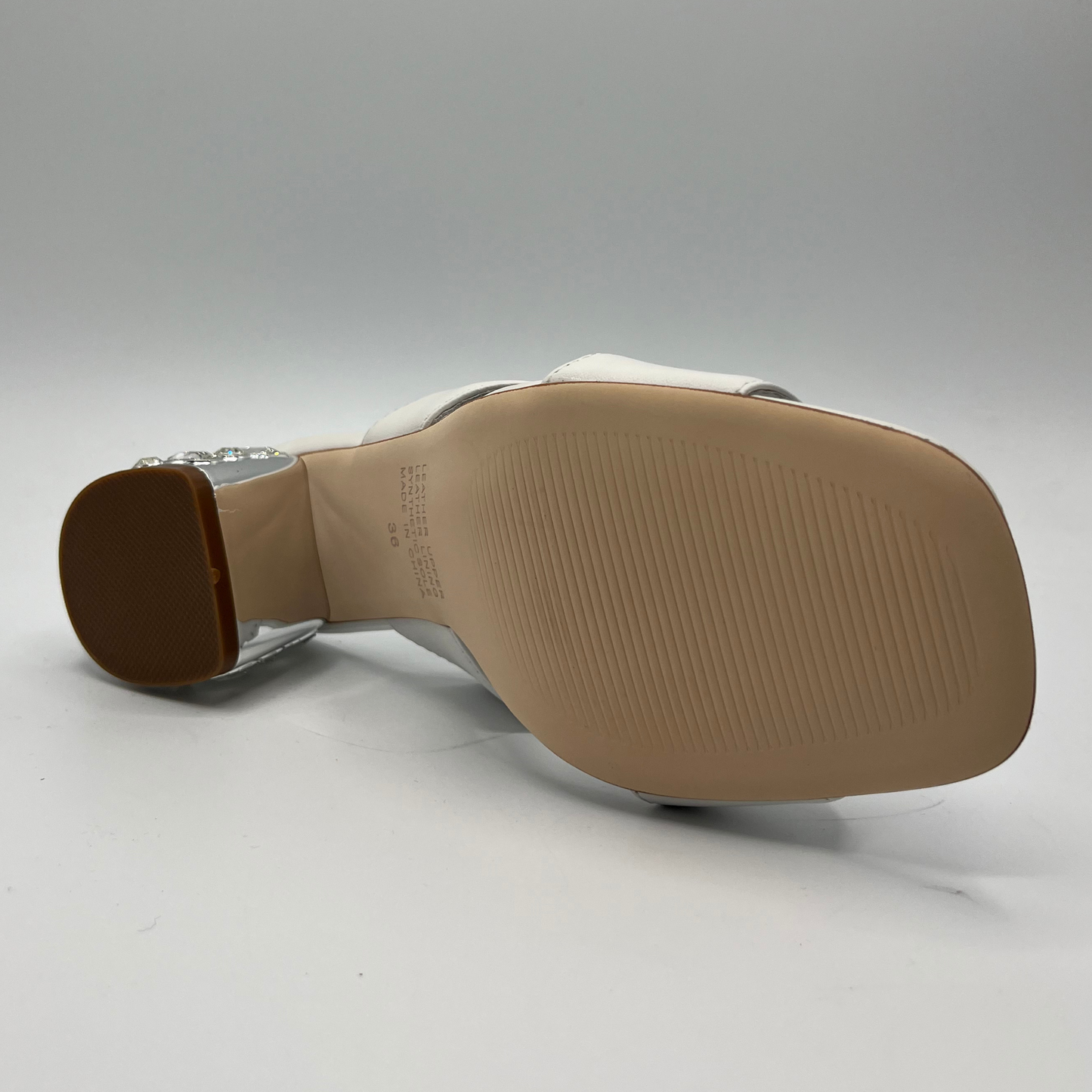 Bottom view of a white leather sandal with a 1/4" bejewelled heel and side cut outs.