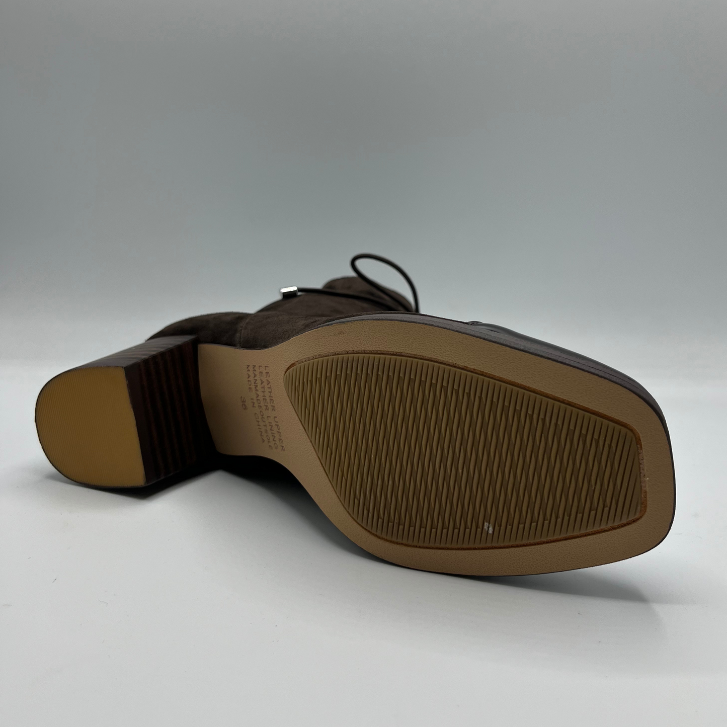 Bottom view of a chocolate leather with a chocolate patent leather toe cap. Stacked heel and unique tie up ankle