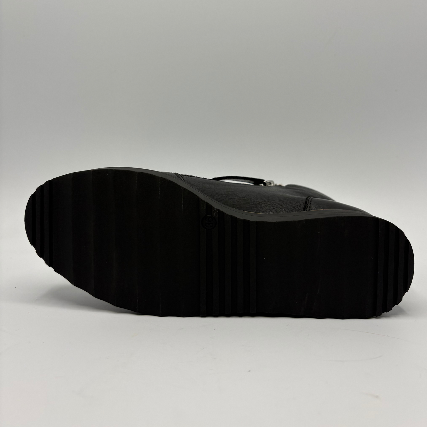 The black textured rubber sole of a boot or shoe, photographed from underneath against a neutral light gray background.