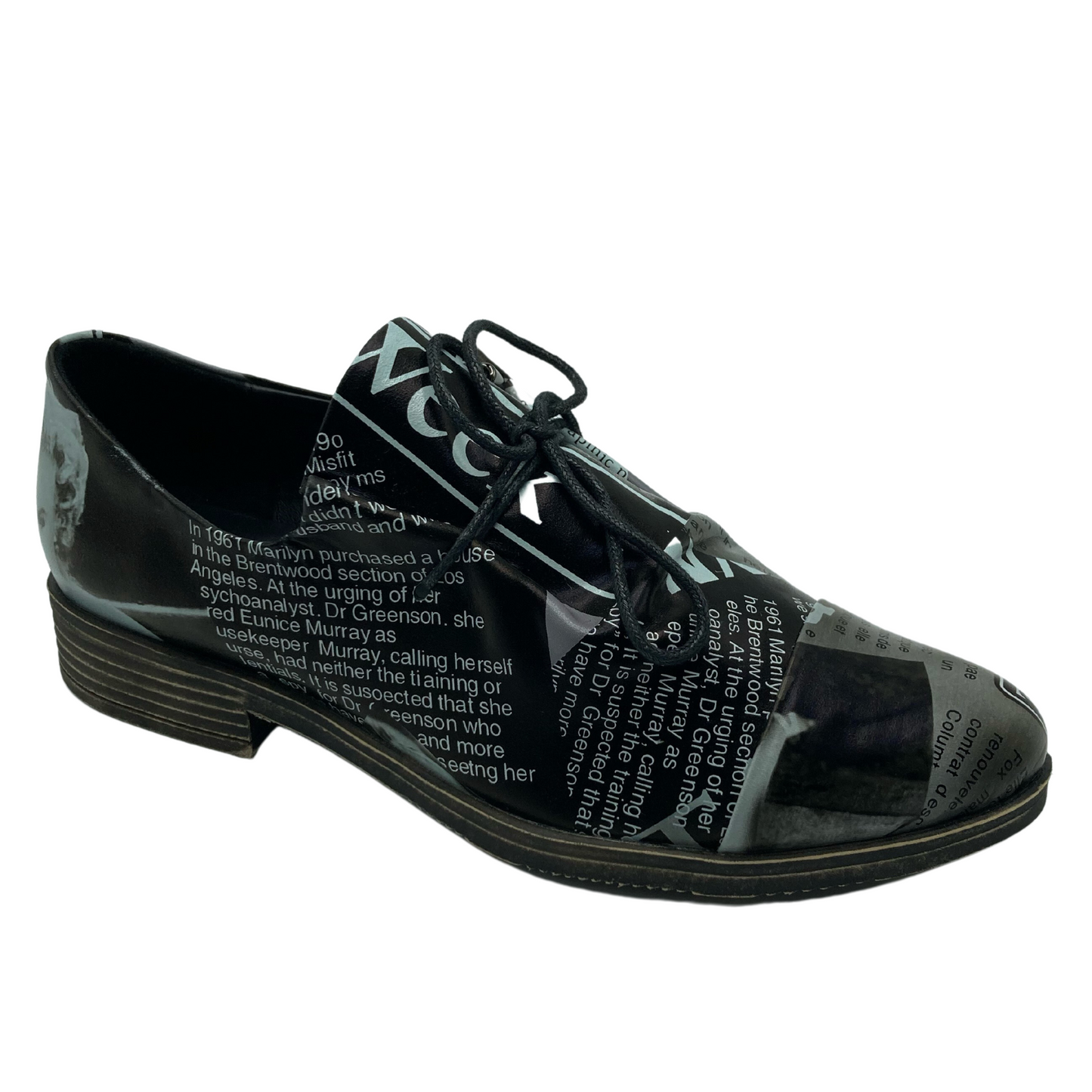 A 45 degree angled view of a leather shoe with a black and white newsprint design on the upper. The laces are black and the sole is a grey brown colour