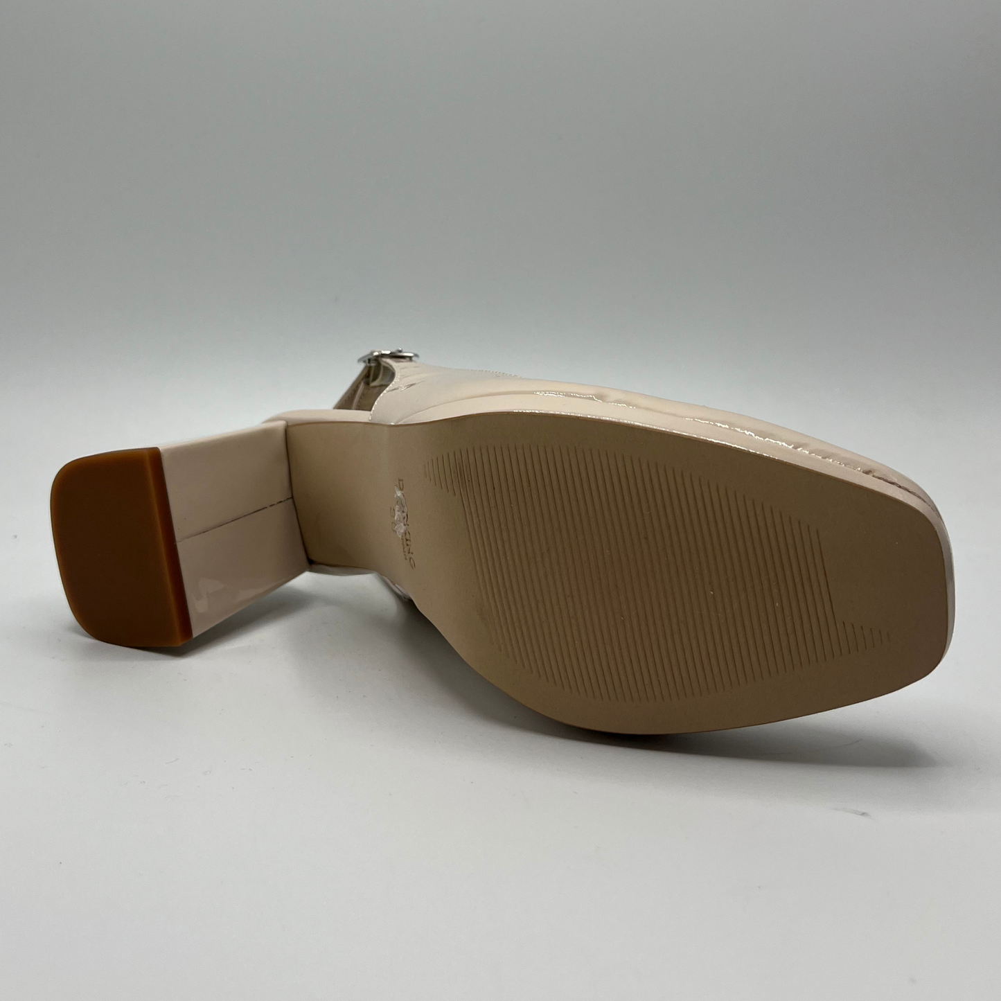 Bottom view of a nude patent leather high heeled shoe with an adjustable sling back strap and a leather insole.