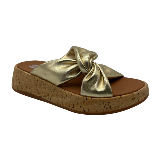 45 degree angled view of gold leather strapped sandal with thick platform sole and knot detail