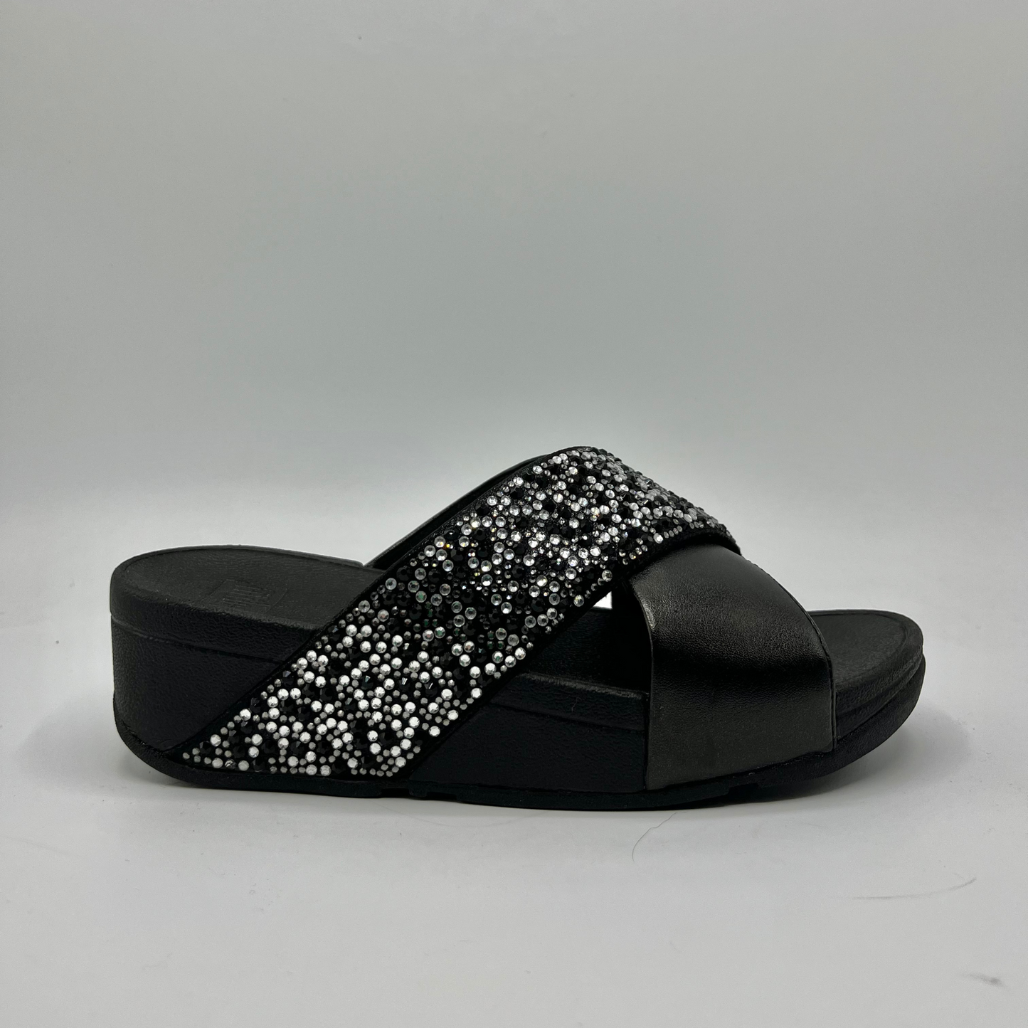 Right facing view of a black wedge sandal with two criss crossed straps, one is covered in small crystals.