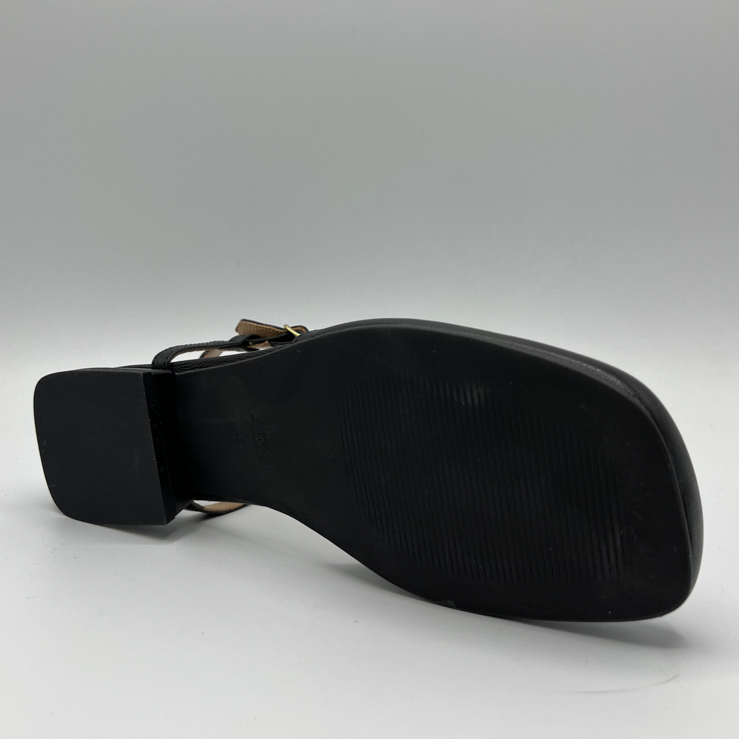 Bottom view of a black leather sandal with a closed toe, an adjustable ankle strap and a low heel.