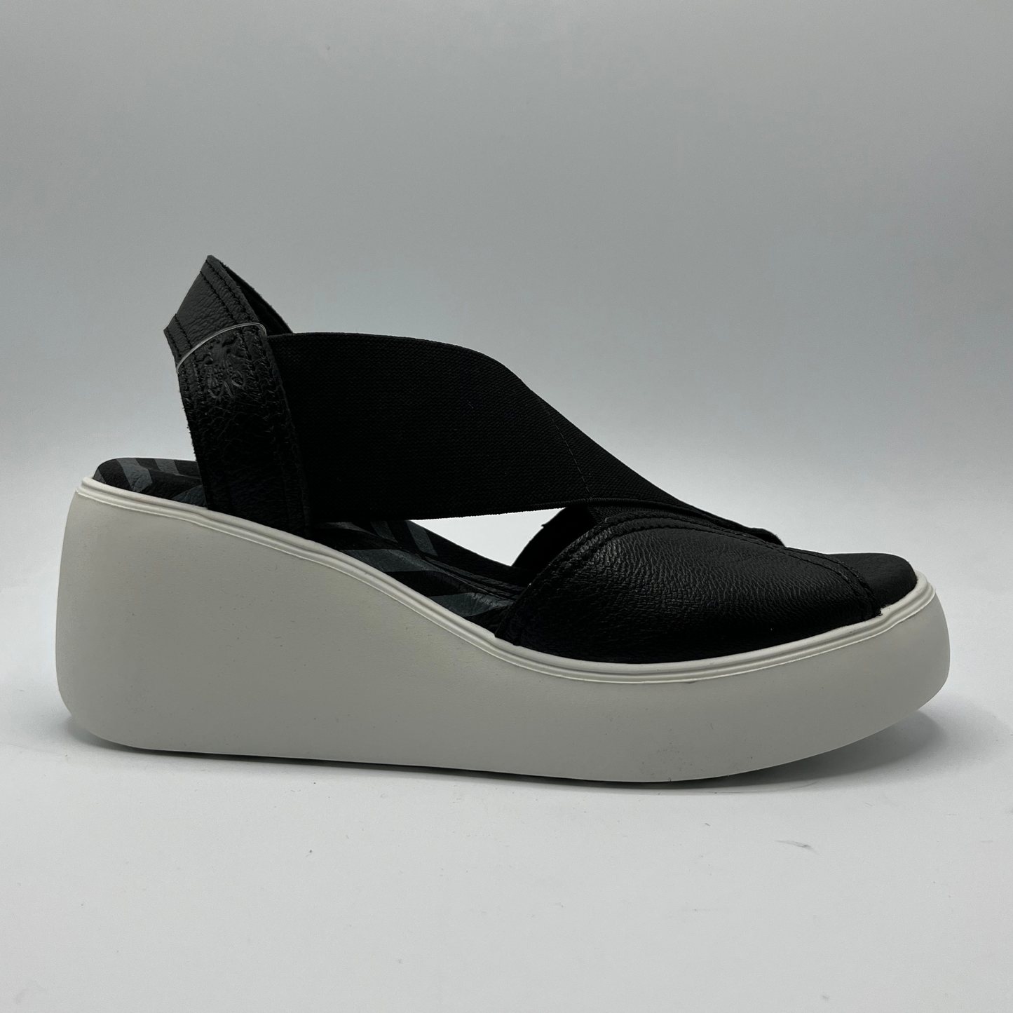 Right facing view of a black leather and elastic strapped sandal with white rubber wedge outsole