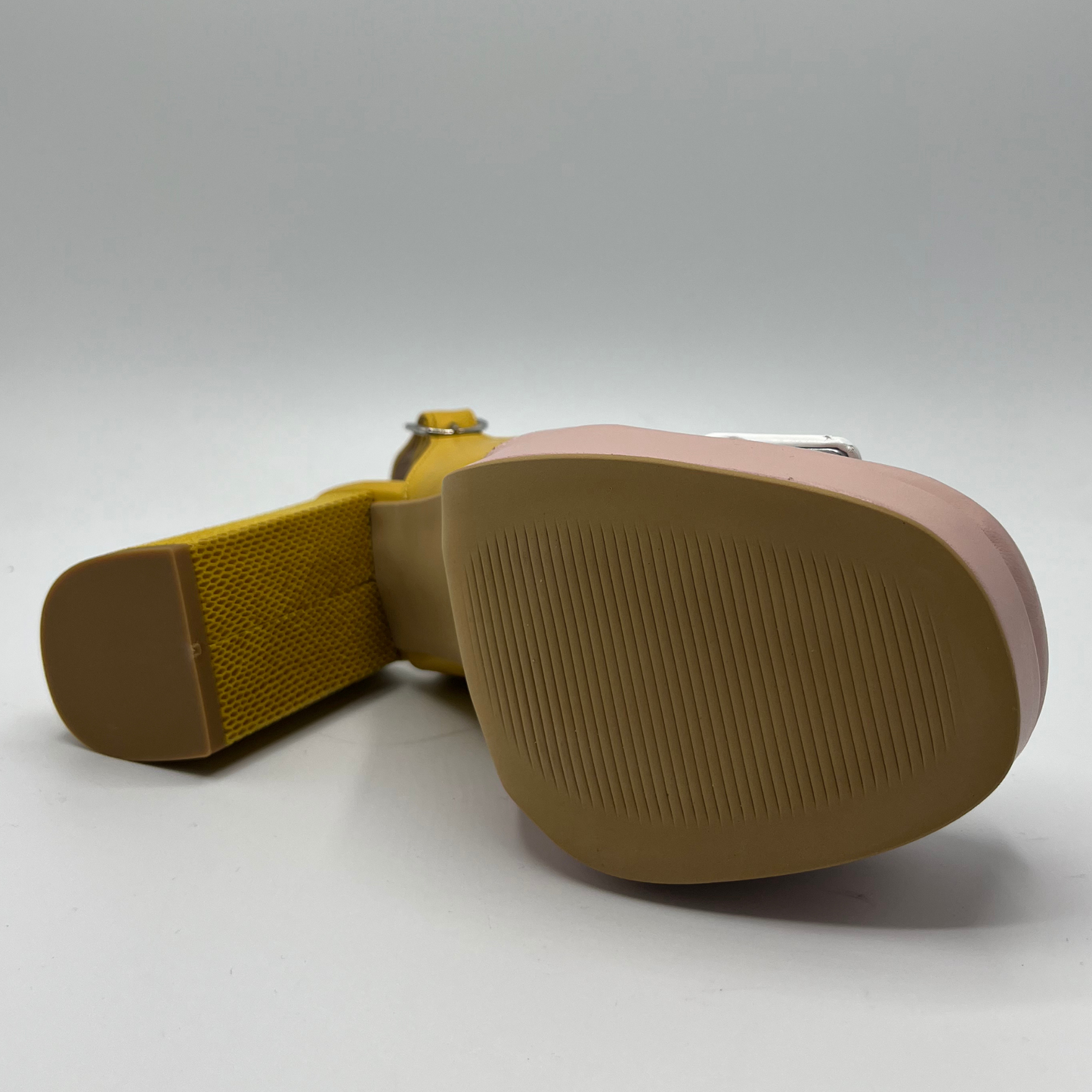 Bottom view of a yellow and pink high heeled shoe with a white buckle detail and an adjustable slingback strap.