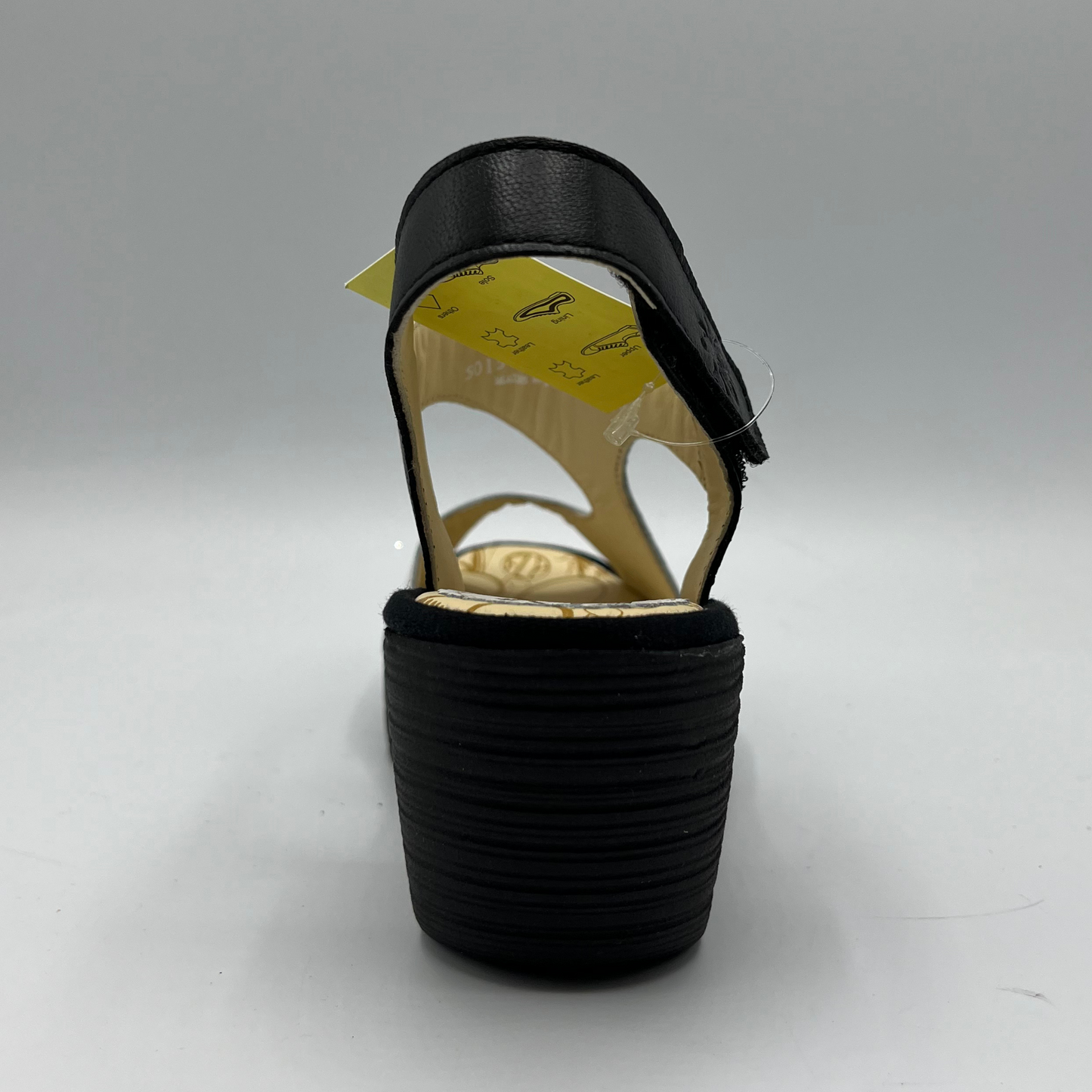 Back view of black and white leather strapped sandal with an adjustable velcro ankle strap and comfortable black wedge heel.