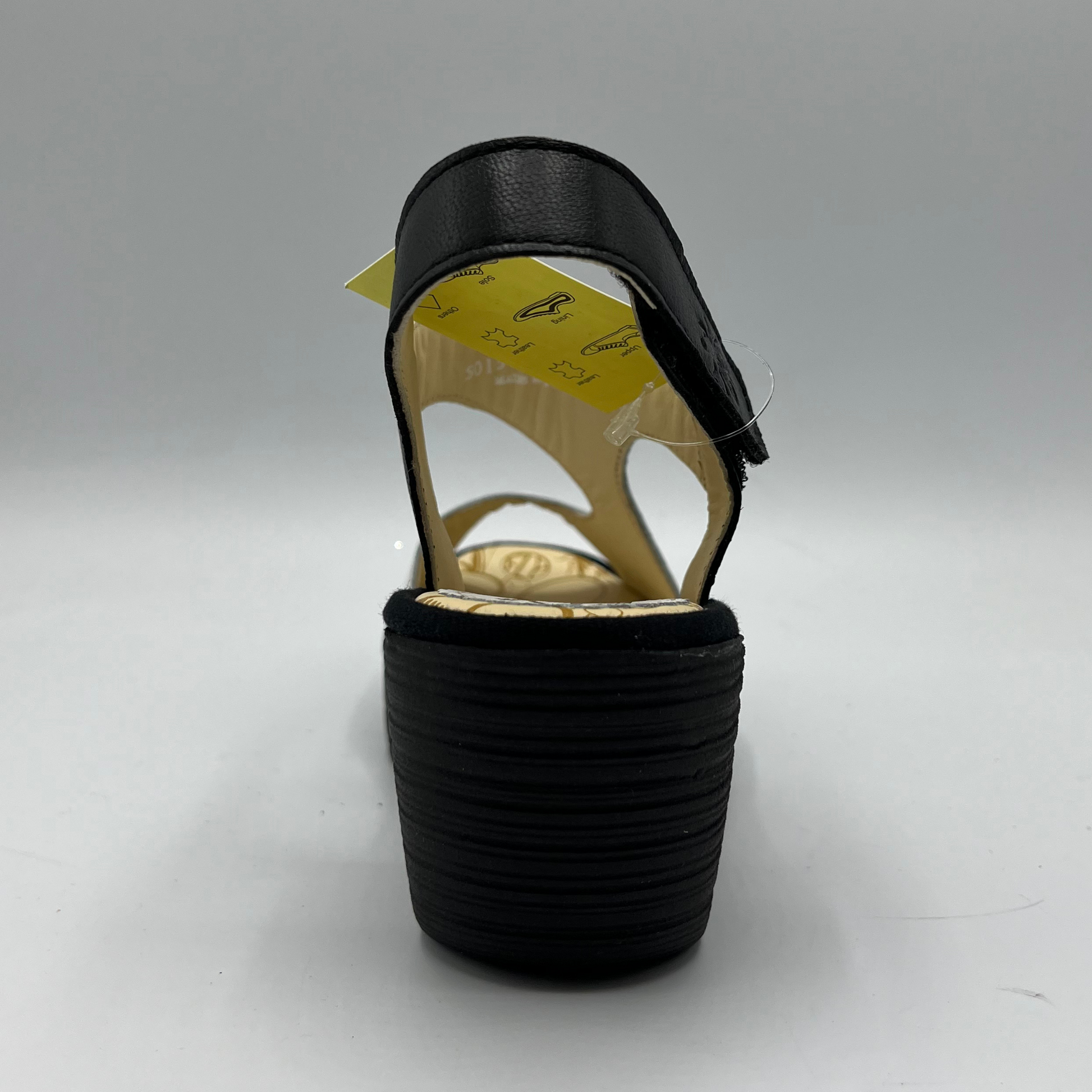 Back view of black and white leather strapped sandal with an adjustable velcro ankle strap and comfortable black wedge heel.