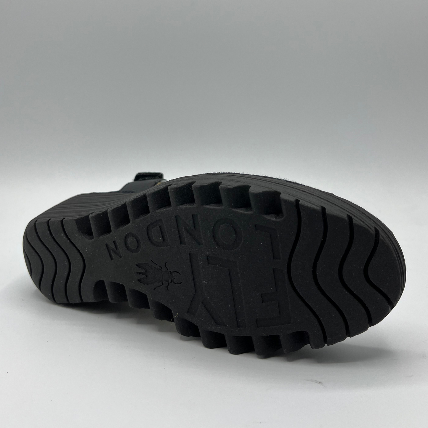 Bottom view of black and white leather strapped sandal with an adjustable velcro ankle strap and comfortable black wedge heel.