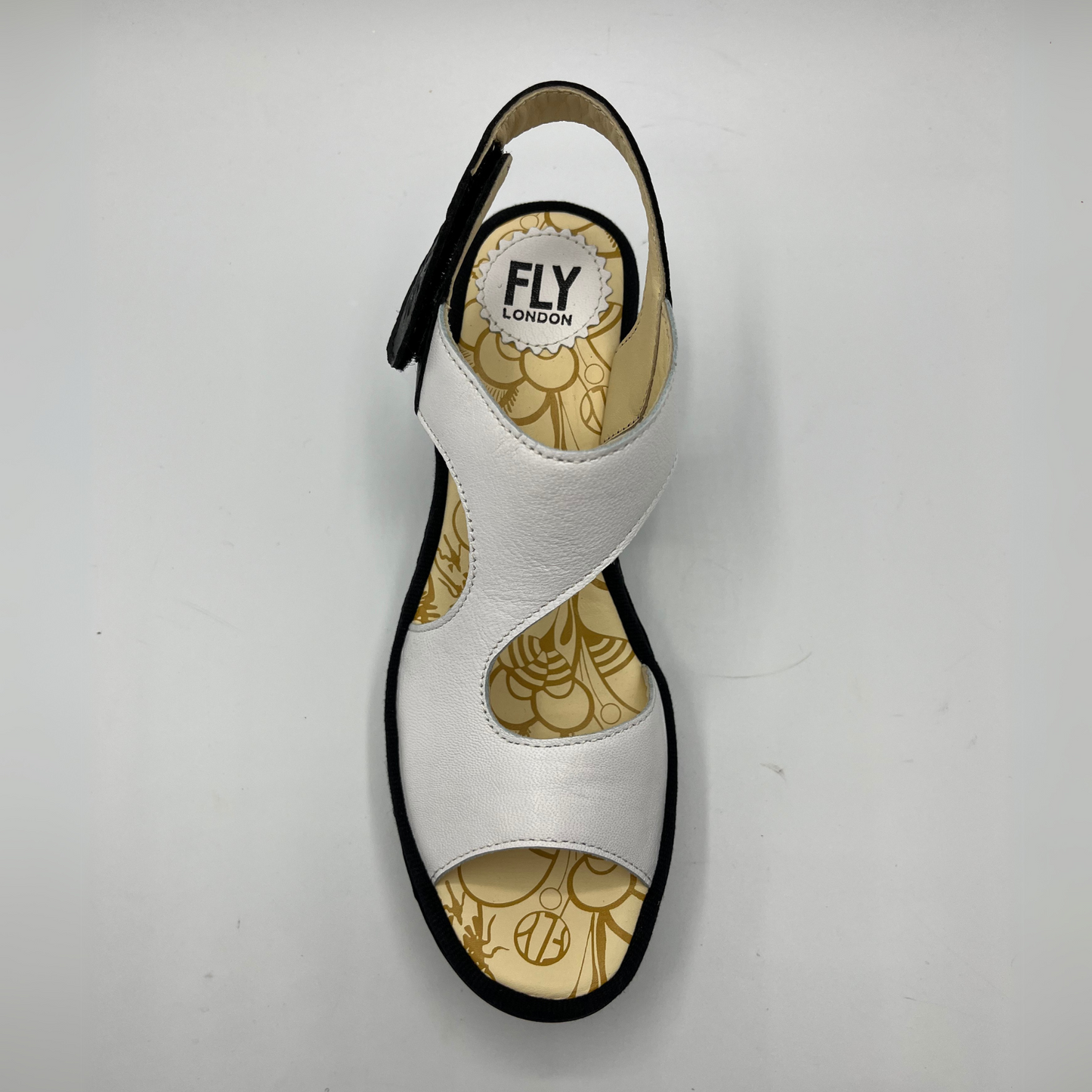 Top view of black and white leather strapped sandal with an adjustable velcro ankle strap and comfortable black wedge heel.