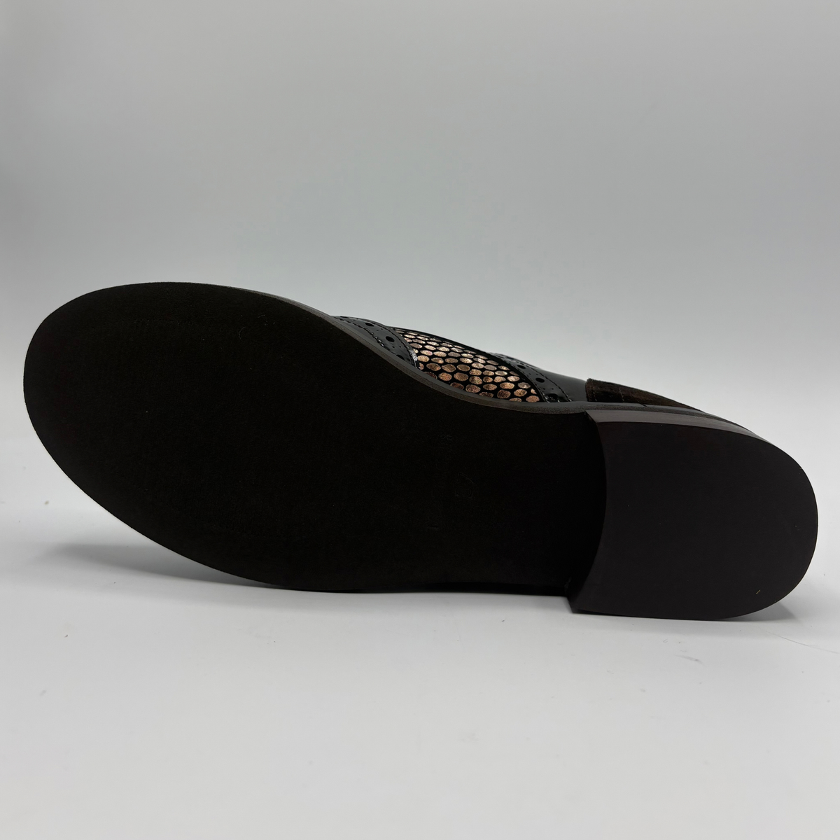 Bottom view of a shoe with a low heel, leather upper and decorative gold buckles on a white background
