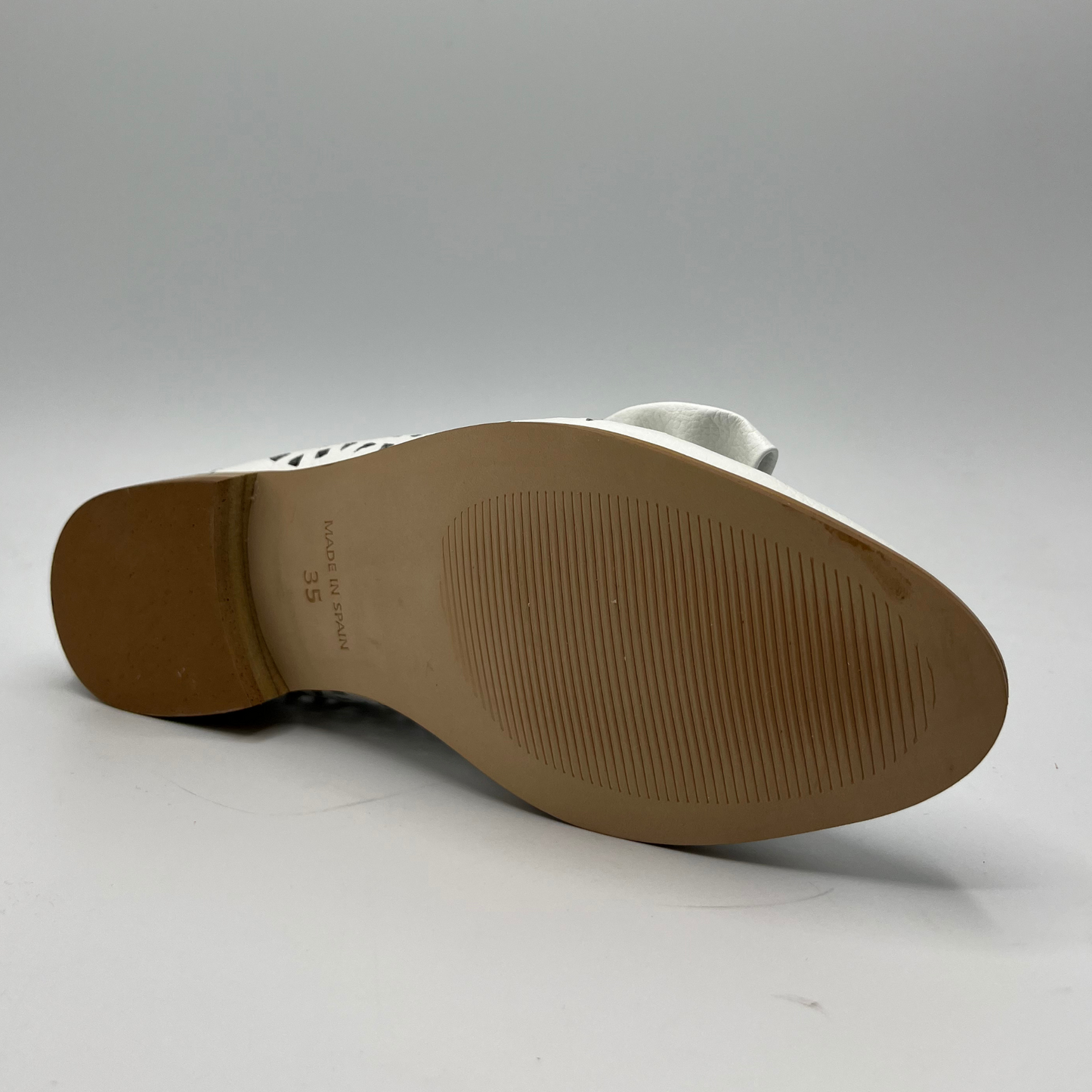 Bottom view of a perforated leather slip on loafer with a low heel and a decorative bow