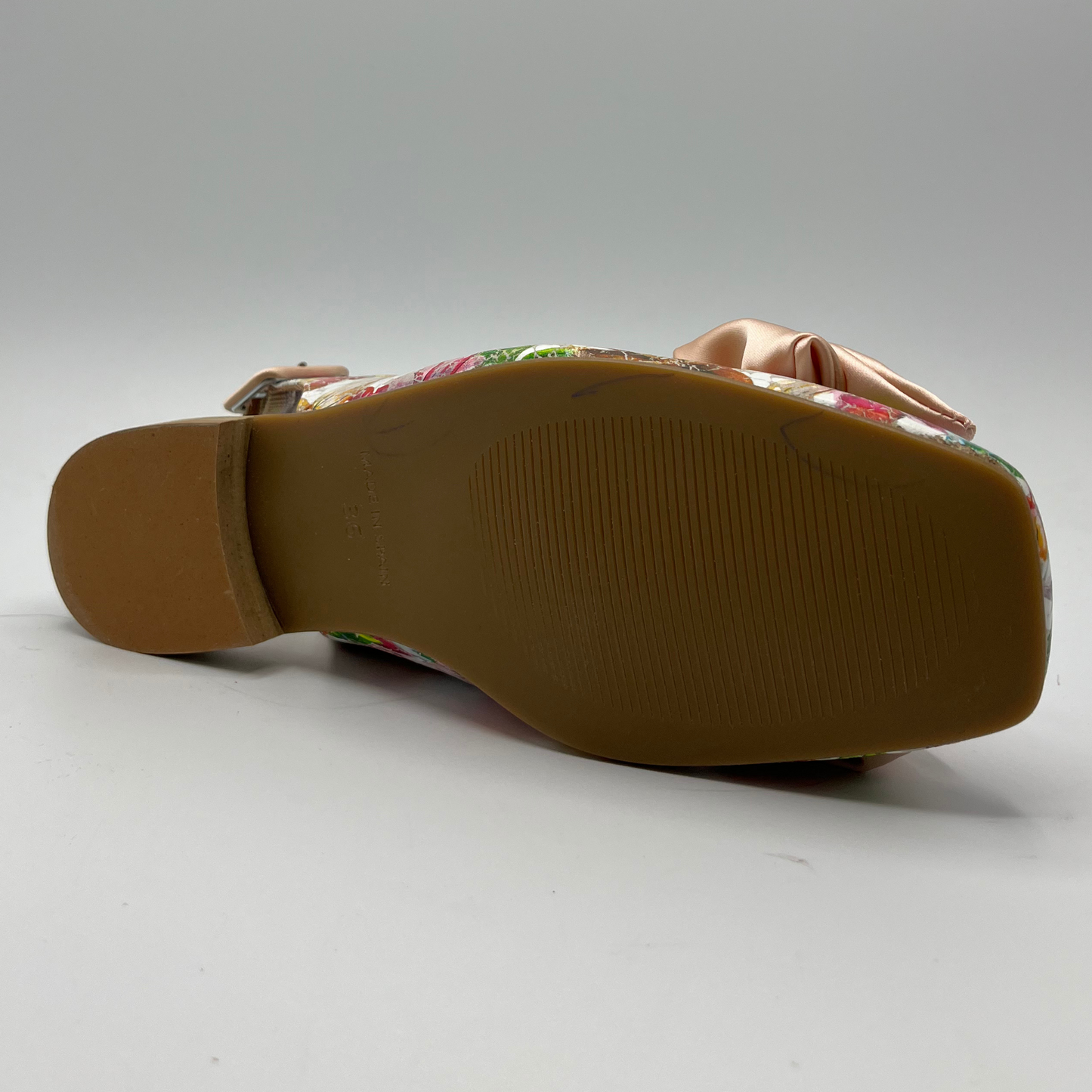 Bottom view of a floral shoe with a short block heel, an adjustable slingback strap and a pink satin bow on the toe.
