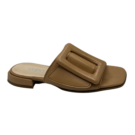 Angled view of brown leather slip on sandals with a low wrapped heel and an oversized buckle detail on strap