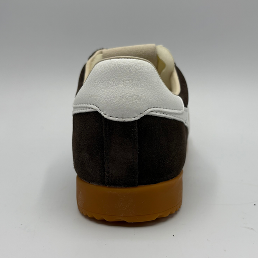 A rear three-quarter view of a low-top sneaker featuring a dark brown suede upper, a white leather heel counter, and a thick brown gum sole, set against a neutral gray background.